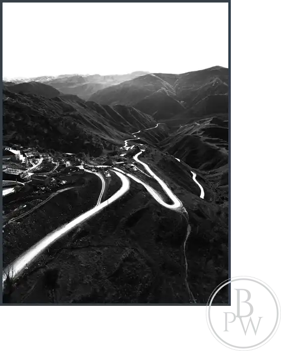 A black and white image of a mountain skyline and a winding road below it.