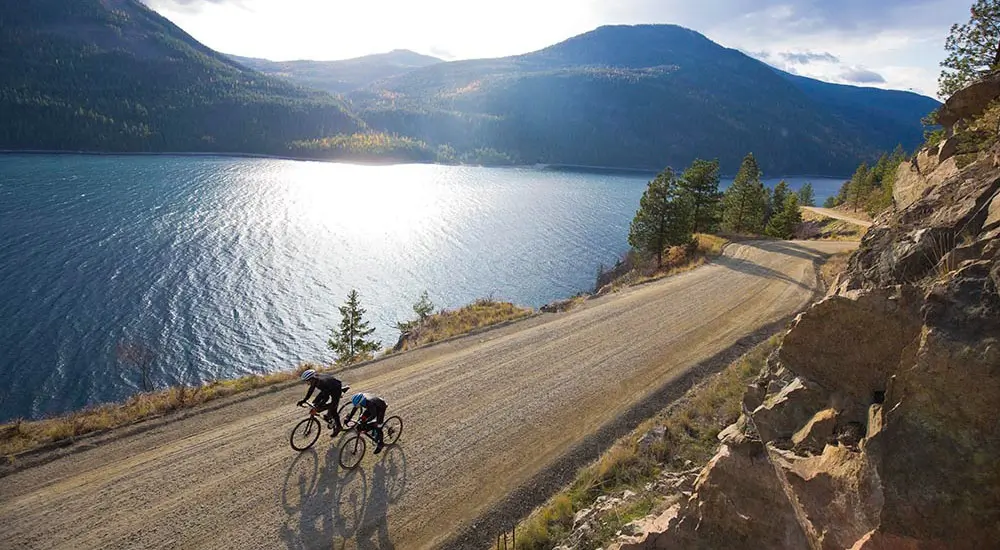 Two people riding a bike beside a river