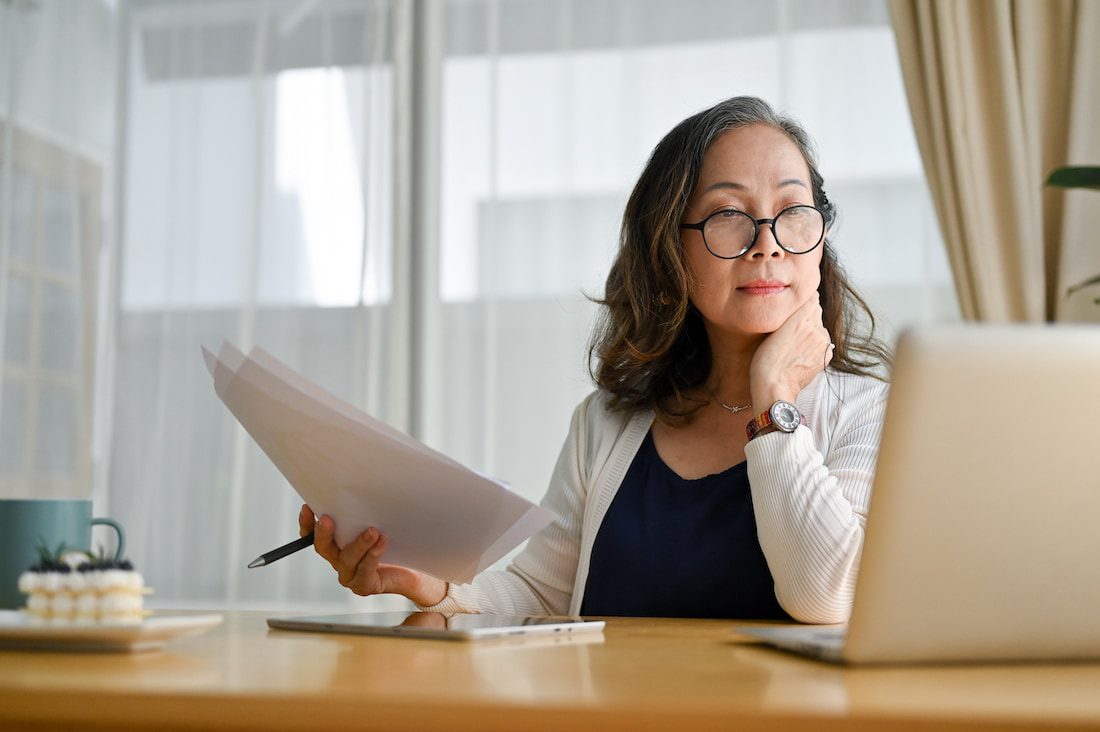 Asian woman with glasses reviewing documents and the 2024 federal budget on her laptop