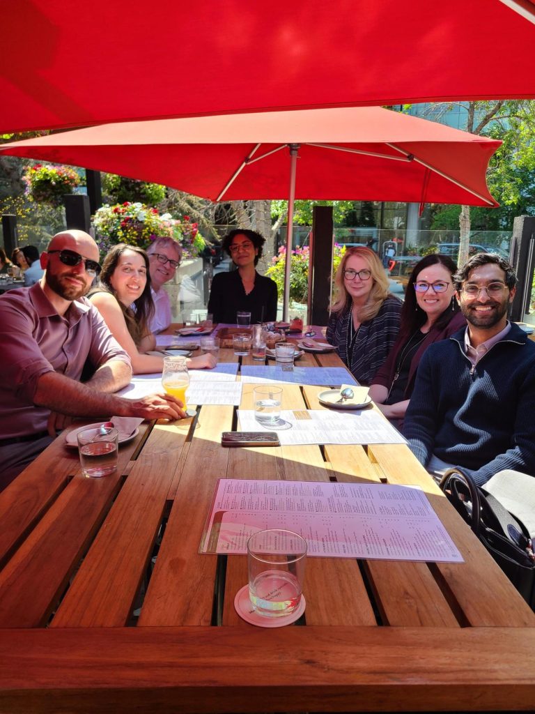 Members of the Wagner Investment Management Team seated outdoors under red umbrellas, celebrating 4 years with Wellington-Altus over lunch.
